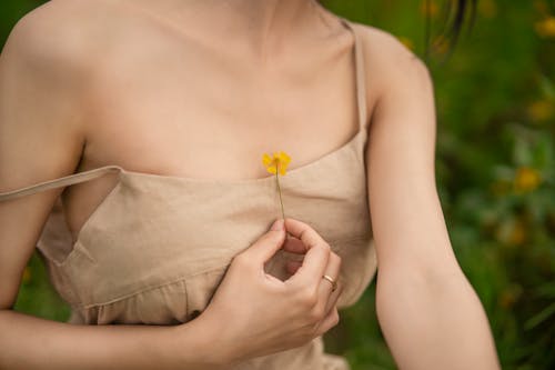 A woman in a tan dress holding a yellow flower