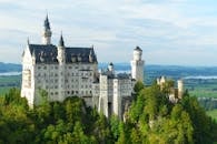 从空中鸟瞰，标志性的新天鹅堡被德国巴伐利亚州郁郁葱葱的绿树环绕