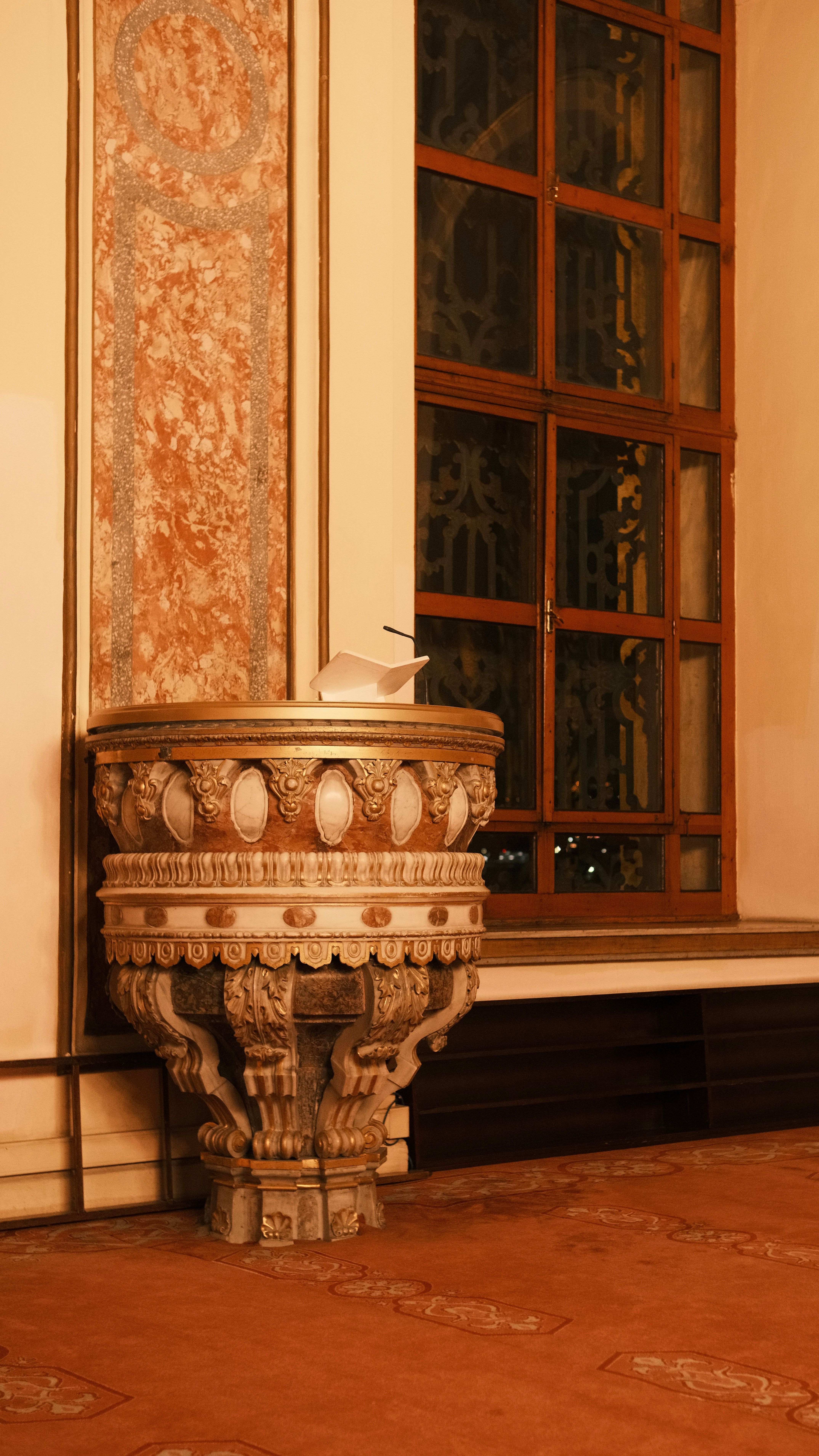 A richly ornamented interior featuring a detailed vase and wooden window paneling.