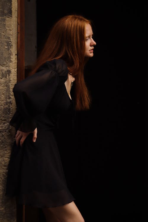 A woman with red hair leaning against a wall