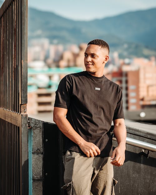 A man in black t - shirt and cargo pants standing on a balcony