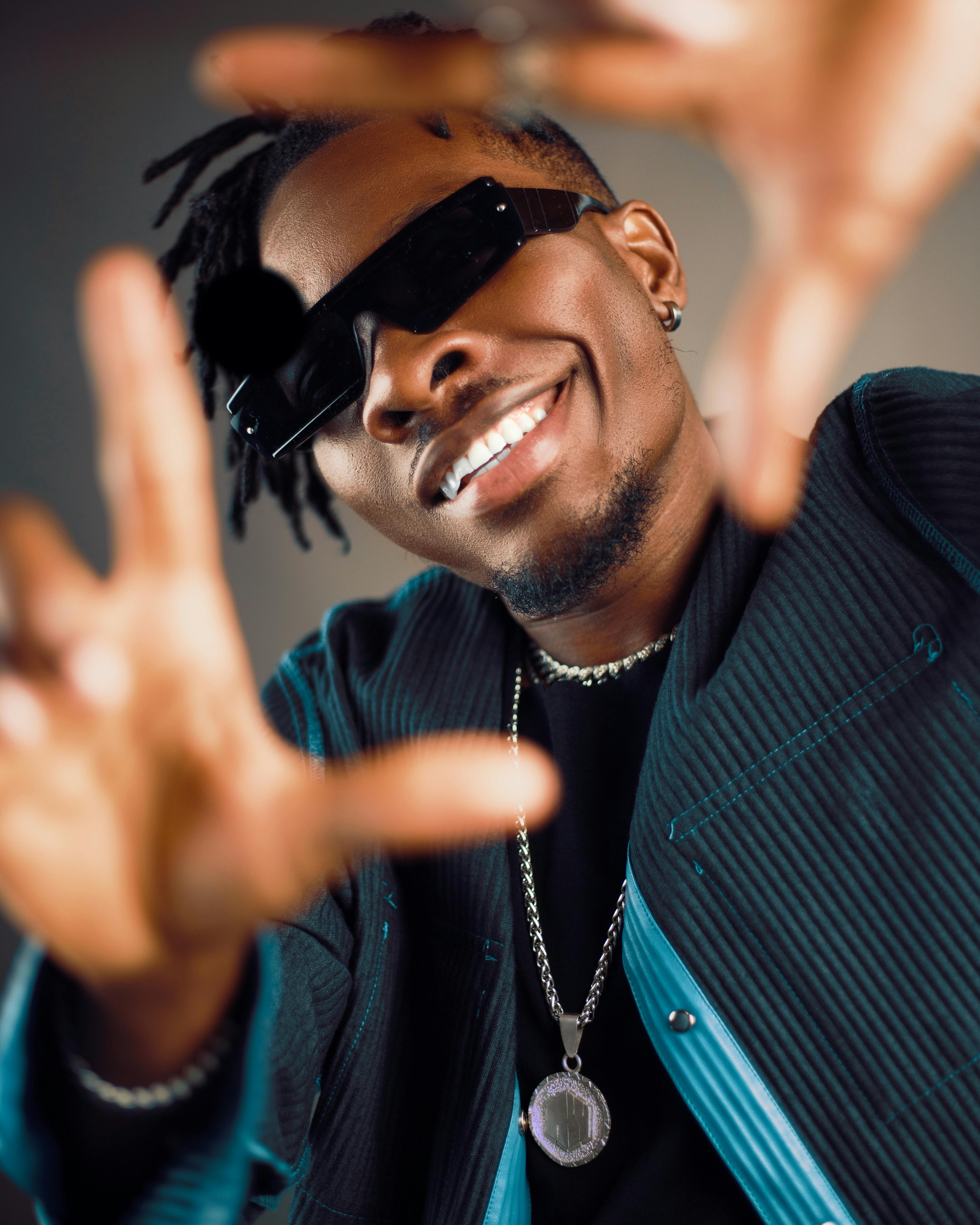 Portrait of a stylish man wearing sunglasses and a necklace, smiling and striking a pose.