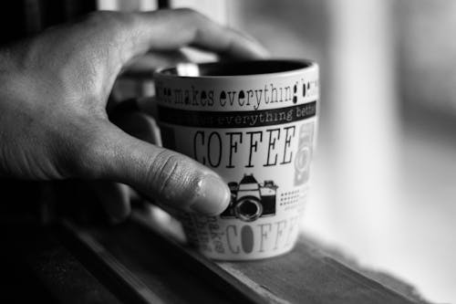 Grayscale Photo of Person Hand Holding Ceramic Cup