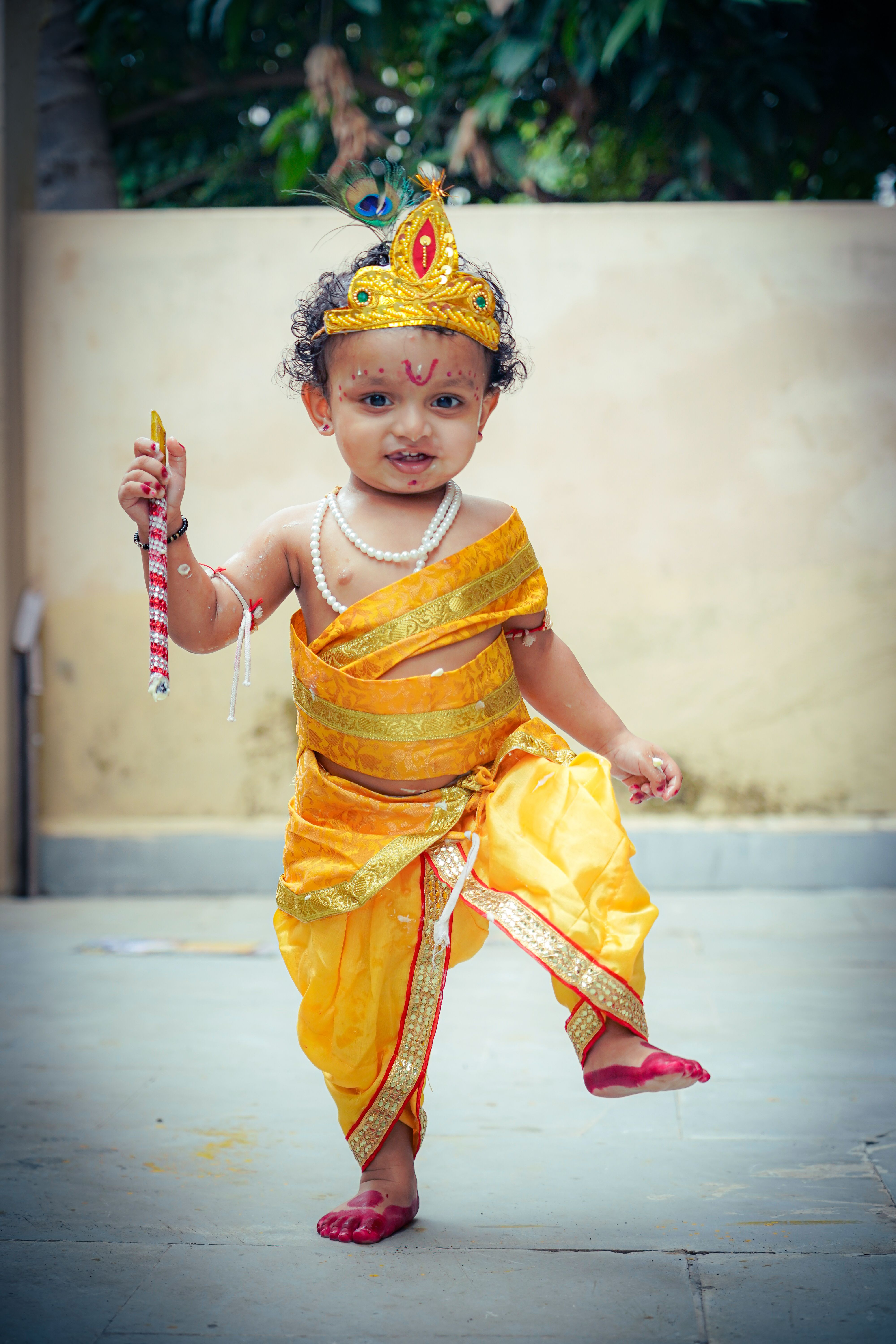 A young child dressed in vibrant Indian traditional clothing with a crown, performing a dance.