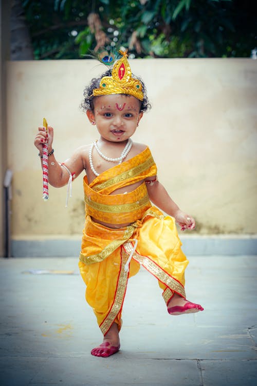 A baby dressed in a yellow outfit holding a stick