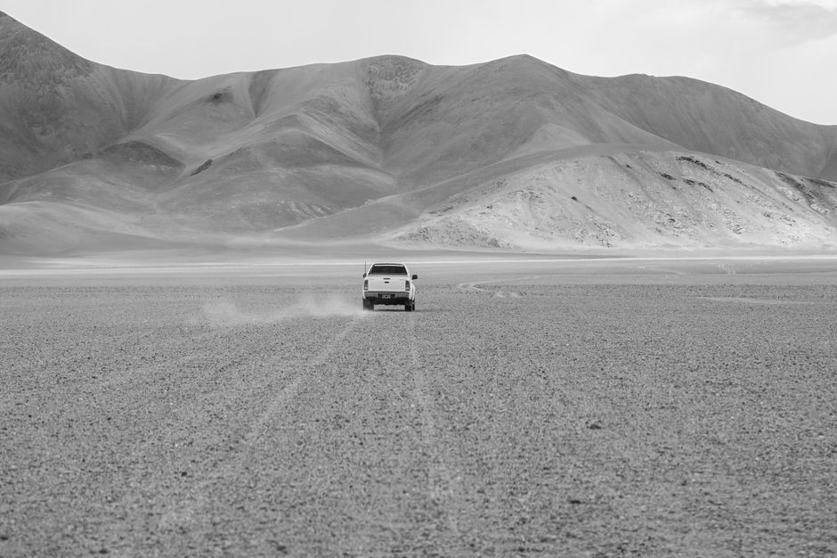 Monochrome capture of a pickup truck driving through a barren desert landscape in Antofagasta de la Sierra, Catamarca.