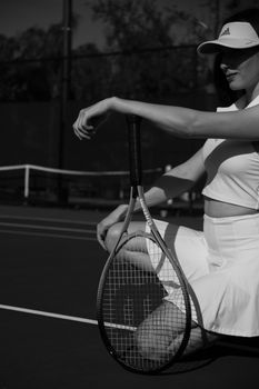 A woman in sportswear kneeling on a tennis court, holding a racket in a black and white photograph.