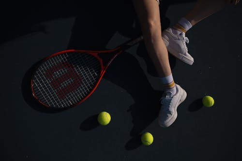 A person's feet and legs are on the ground with tennis balls