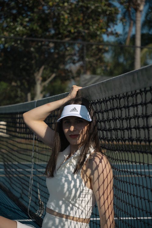 A woman in white tennis outfit leaning against a tennis net