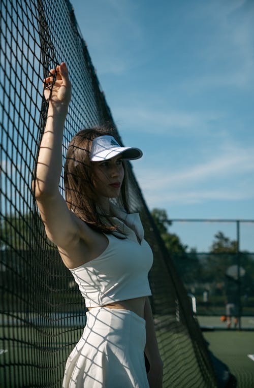 A woman in a white hat and white tennis skirt standing on a tennis court