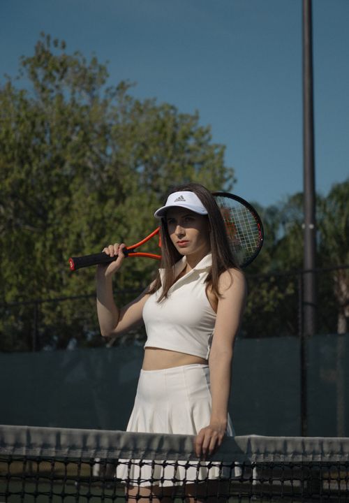 Free A young woman in sportswear stands by a tennis net with a racket, under a clear sky. Stock Photo