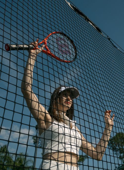 Free Woman in sportswear holding a tennis racket against a net on a sunny day outdoors. Stock Photo