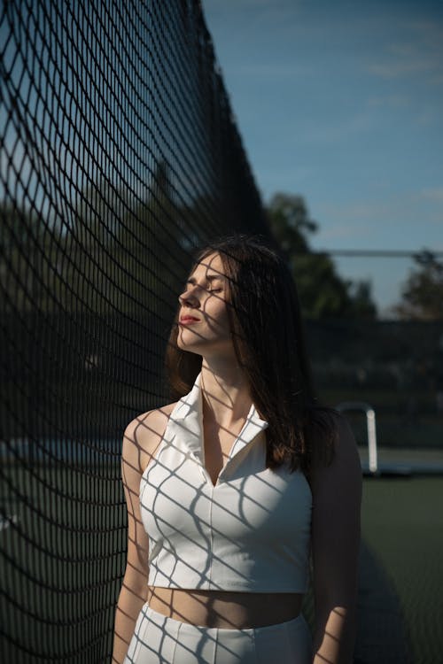 Free A woman in white standing in front of a tennis net Stock Photo