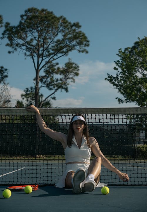 A woman sitting on a tennis court with tennis balls