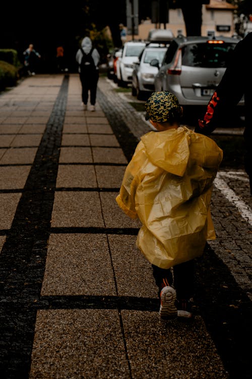 A child wearing a yellow raincoat walking down a sidewalk
