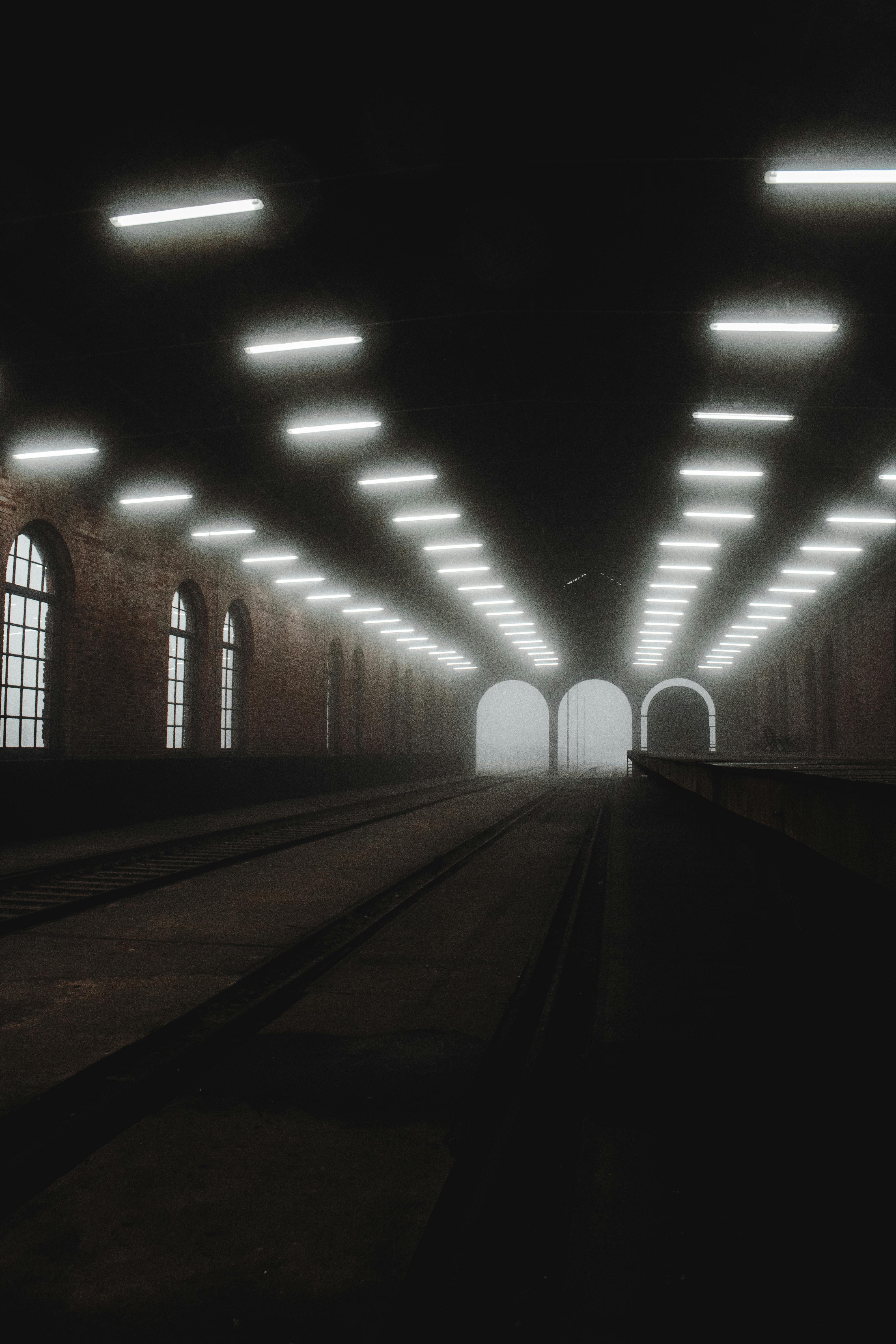 Dark and atmospheric view of an empty railway station interior illuminated by overhead lights.