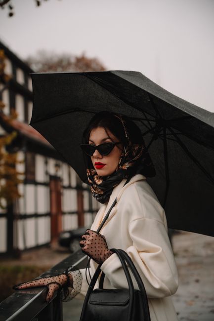 Stylish woman in coat and gloves holding an umbrella, embodying elegance and fashion.