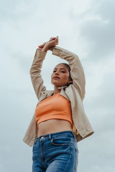 Portrait of a stylish woman posing confidently outdoors against a cloudy sky.