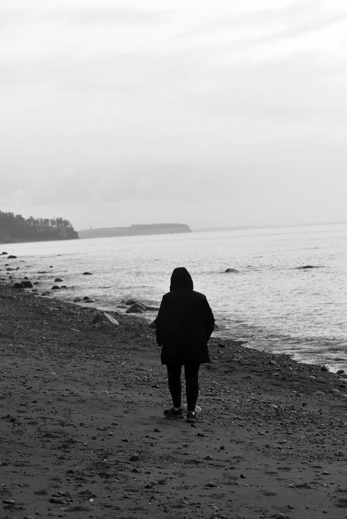 Free A solitary person walks along a desolate beach under a cloudy sky. Stock Photo