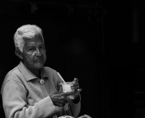 Free Portrait of an elderly woman holding a drink with a straw, in black and white. Stock Photo