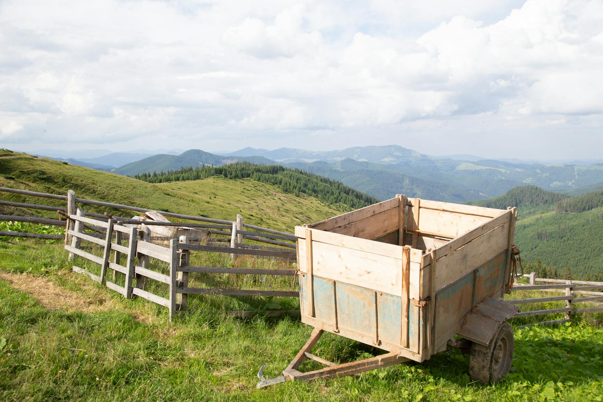 Wooden trailer on a lush, rural hillside with distant rolling hills under a bright sky.