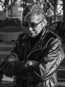 Black and white portrait of a fashionable man in a leather jacket standing outdoors in Tokyo.