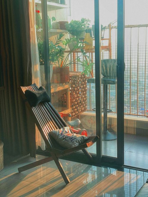 Free Inviting balcony space with plants, a wooden chair, and a cityscape in sunlight. Stock Photo