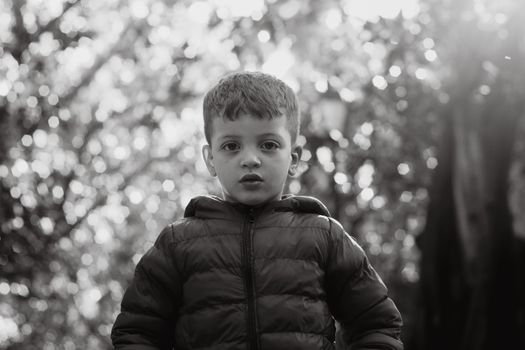 A striking black and white portrait of a young boy wearing a jacket, outdoors.