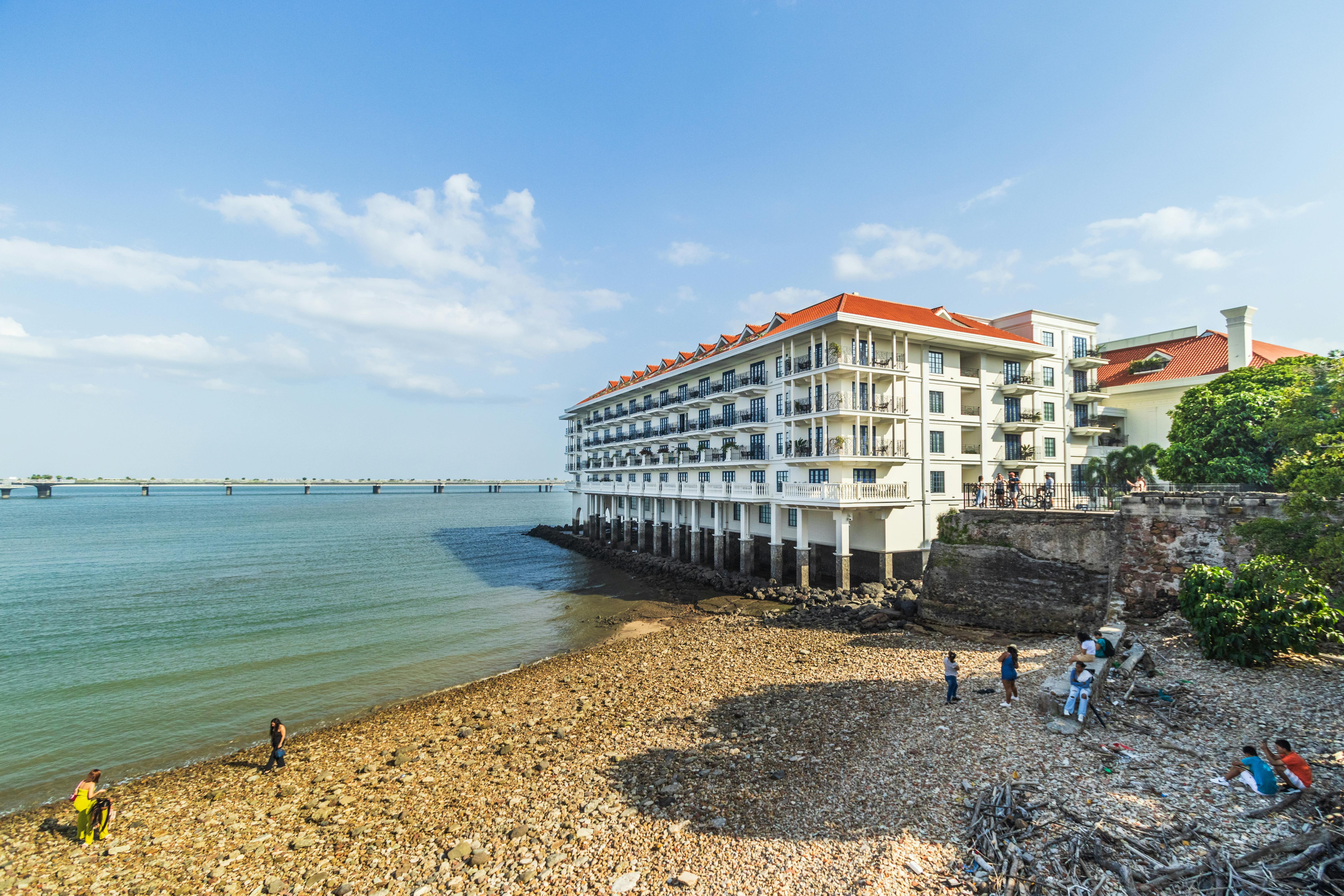 A scenic view of a colonial style hotel by the beach in Panama City with people enjoying the shore.