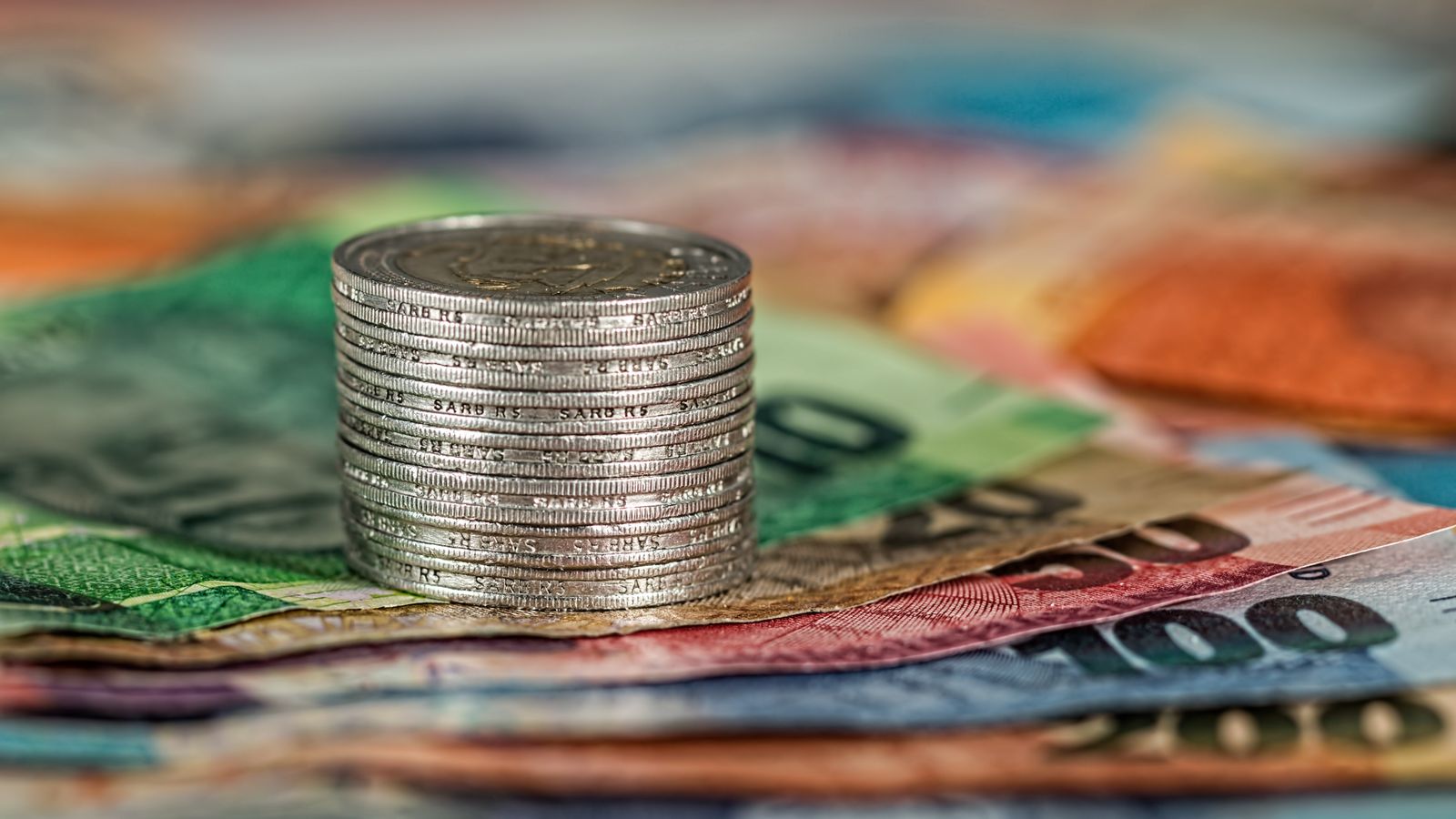 A stack of coins on top of various colored banknotes, symbolizing finance and currency.