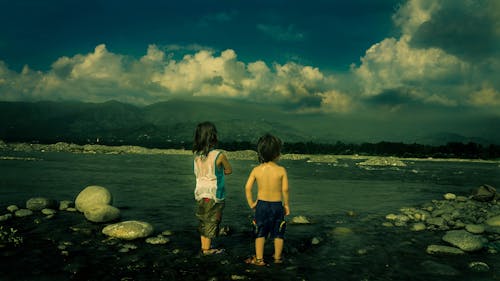 Ребенок в белой майке рядом с ребенком в черных шортах у моря в дневное время