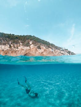 A serene over-under photograph capturing a diver exploring the turquoise waters off the coast of Sardinia, Italy. by Symeon Ekizoglou