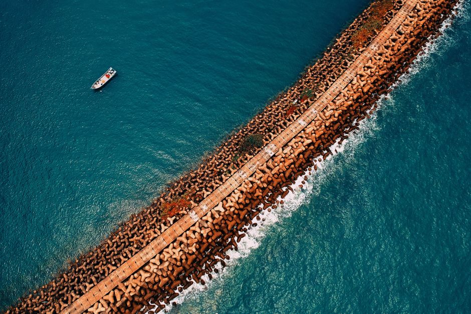 Aerial shot of a rocky breakwater with a lone boat on the ocean, showcasing coastal beauty.