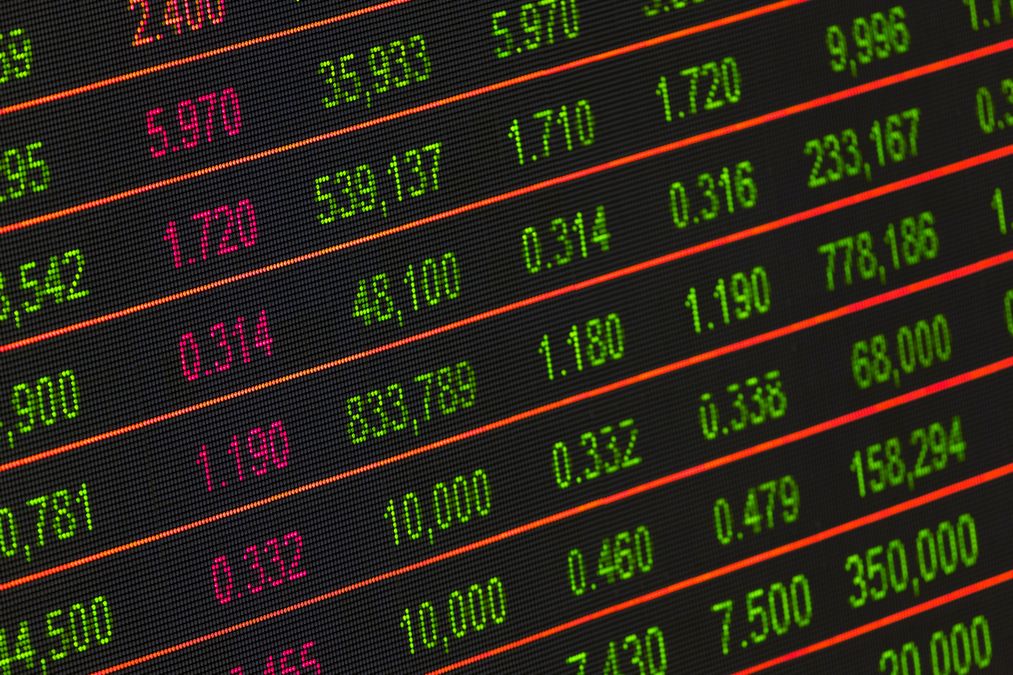 Painel eletrônico de bolsa de valores exibindo cotações e variações de ações em cores