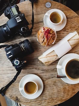 俯视木桌，上面摆着咖啡、零食和单反相机，展现了食物与摄影的完美融合