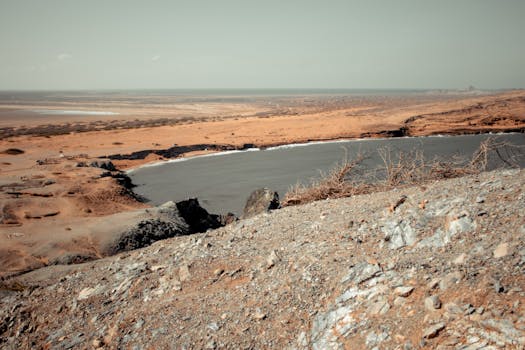 Scenic desert landscape featuring rocky terrain, sparse vegetation, and a serene lake under daylight.