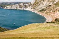 海岸线景色优美，悬崖、沙滩与海上孤独的帆船构成一幅画卷