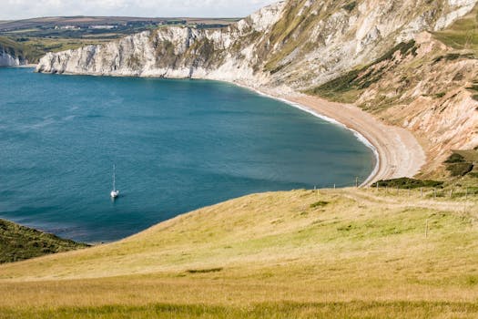 海岸线景色优美，悬崖、沙滩与海上孤独的帆船构成一幅画卷