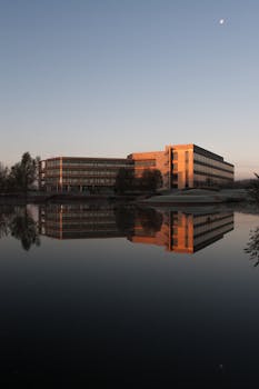 日落时分，一座现代化的办公楼倒映在晴朗天空下的平静湖面上
