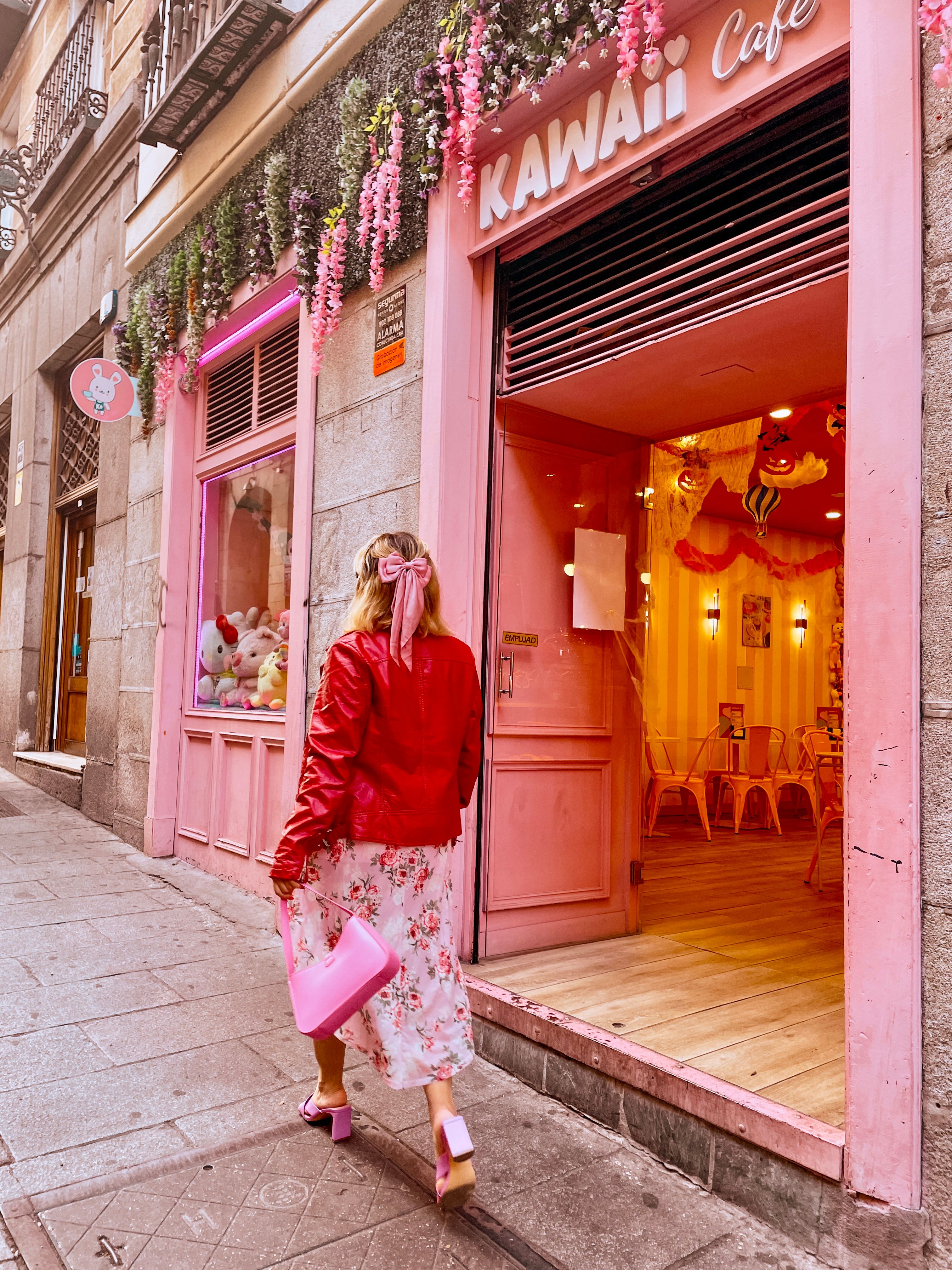 Stylish woman with pink accents walking past Kawaii Cafe decorated with florals.