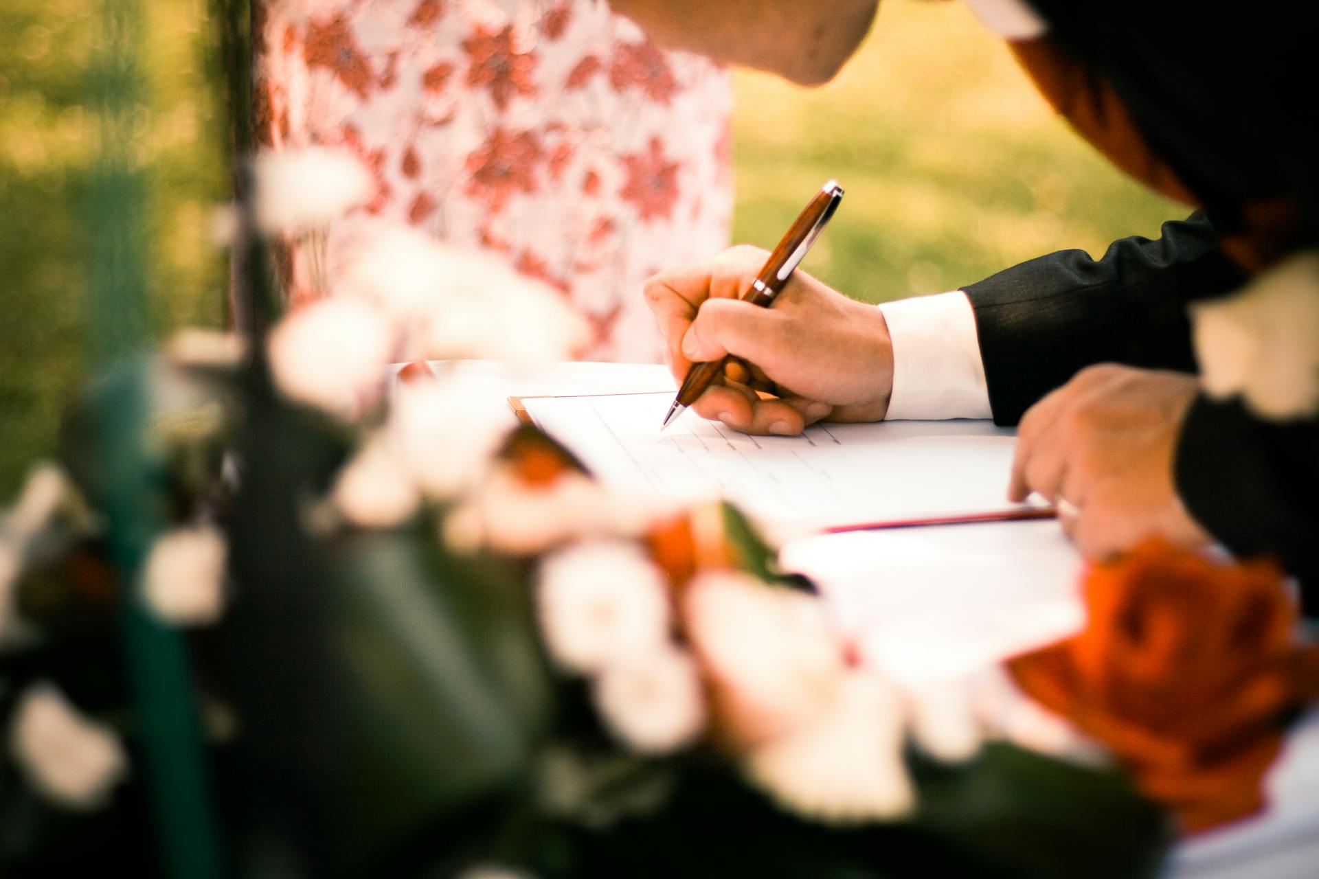 A close-up of hands signing a marriage contract during an outdoor wedding ceremony