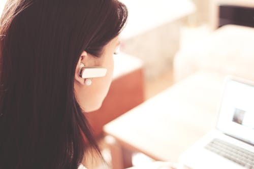 Woman Wearing Earpiece Using White Laptop Computer