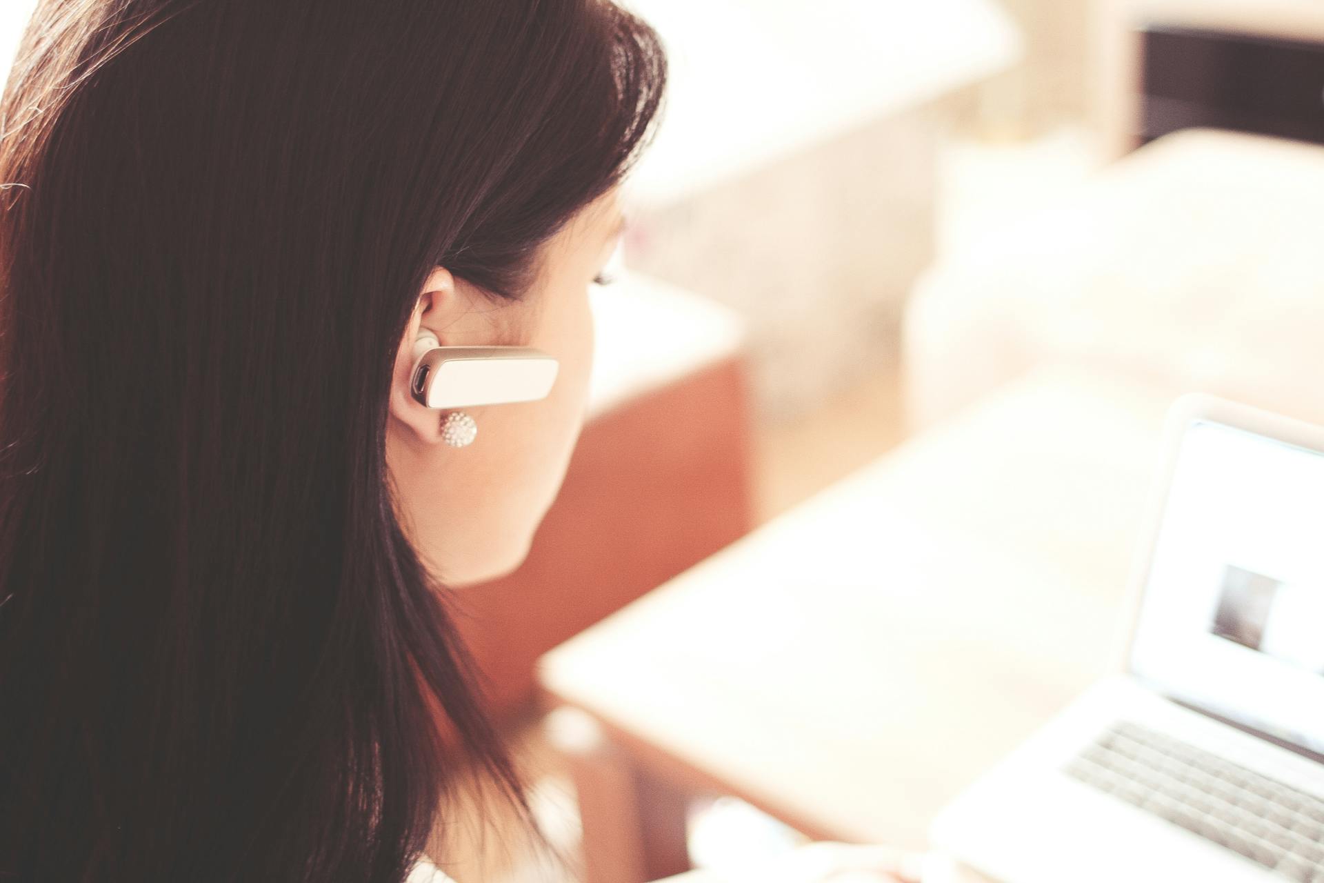 A businesswoman using a Bluetooth headset while working on her laptop in a modern office.