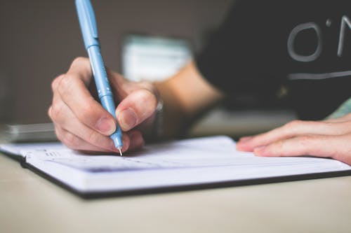 Pessoa Segurando Uma Caneta Esferográfica Azul Escrevendo No Caderno