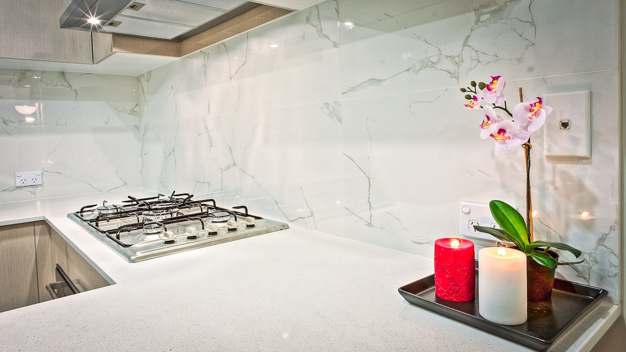 Two Light Red and White Pillar Candles Beside Pink Orchid Flowers in Kitchen