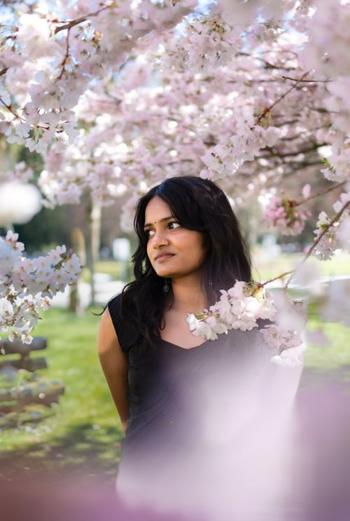 Free A contemplative woman stands surrounded by blooming cherry blossoms in a Vancouver park. Stock Photo