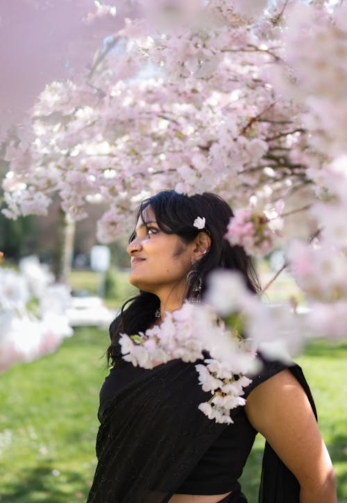 A woman in a black sari standing under a tree with pink blossoms