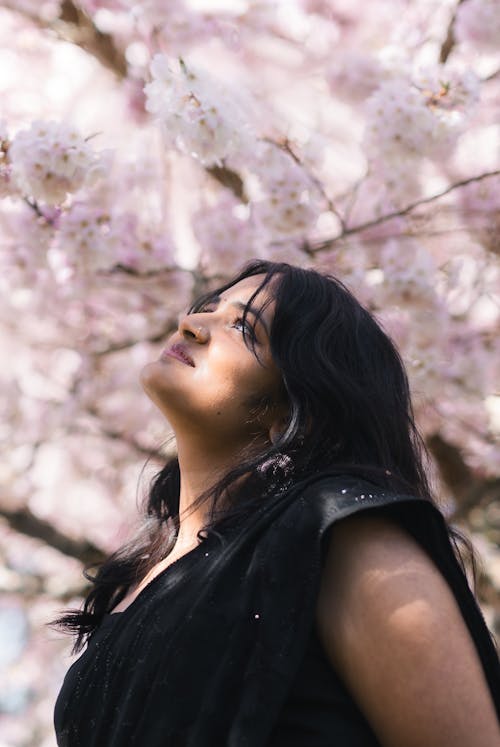 A woman in black standing under a tree with pink blossoms