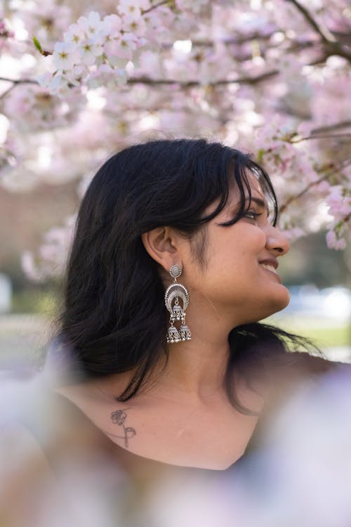 A woman wearing earrings and a necklace standing in front of a tree