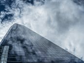 从低角度仰望，一座高耸的现代摩天大楼的玻璃窗反射着云彩，映衬着戏剧性的天空